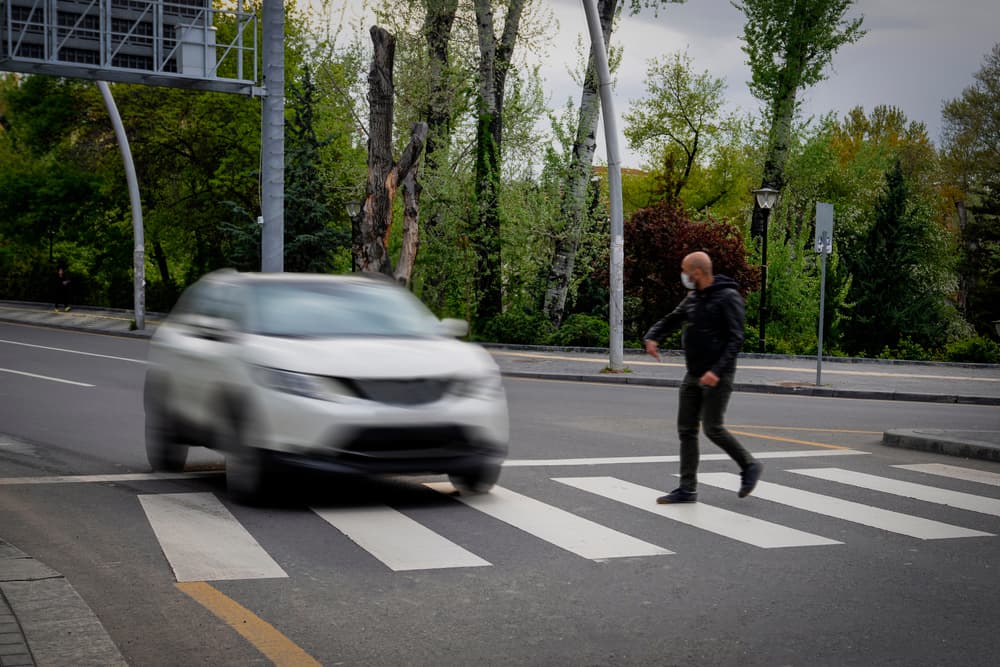 A pedestrian on intersection in front of a speedy car